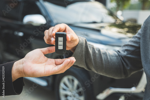 Close up businessman in suit his hands showing or giving car key for customer getting new car. Buy sell rent car concept.