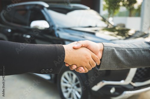 Fotografie Two businessmen made a deal to buy a used car, he made a contract and stood shaking hands in front of the car