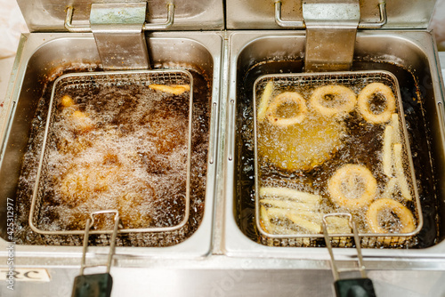 Snacks are fried in a deep fryer. Onion rings and potatoes are fried in oil.