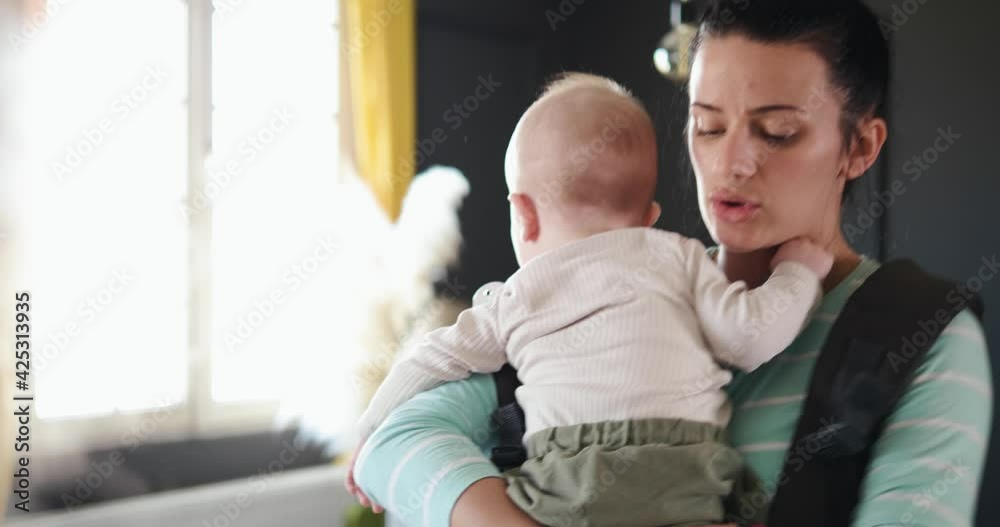 Young worried mother is rocking a crying baby while cooking lunch. 