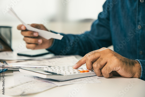 Young man was using a calculator to calculate his income and expenses. In his hand there were bills to pay a lot in debt.