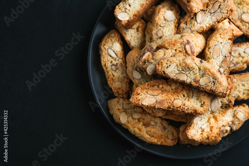 Cantuccini biscotti with almonds on a black plate on a dark background top view copy space close-up.