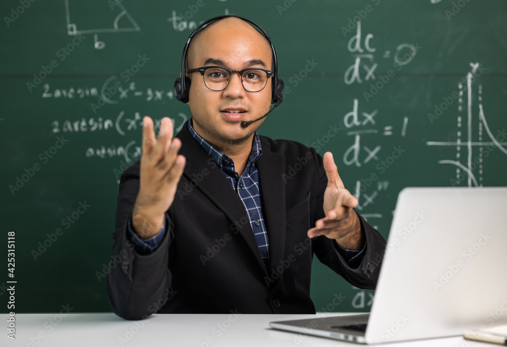 Indian young teacher man looking at camera sitting teaching online video conference live stream. Asian teacher wearing headset teaching class webinar online for students learning. Indian young teacher man looking at camera sitting teaching online video conference live stream. Asian teacher wearing headset teaching class webinar online for students learning.