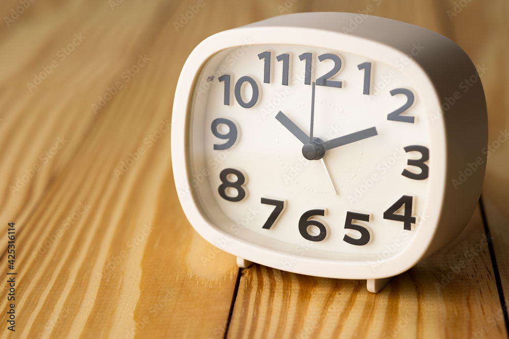 Small white alarm clock, black numbers, set the time for 10.10 o'clock, placed on a wood table. Small white alarm clock, black numbers, set the time for 10.10 o'clock, placed on a wood table.
