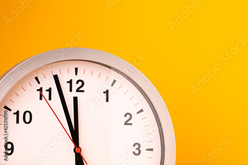 Large white alarm clock, black numbers, set the time placed on a table. Clock on isolated yellow background.