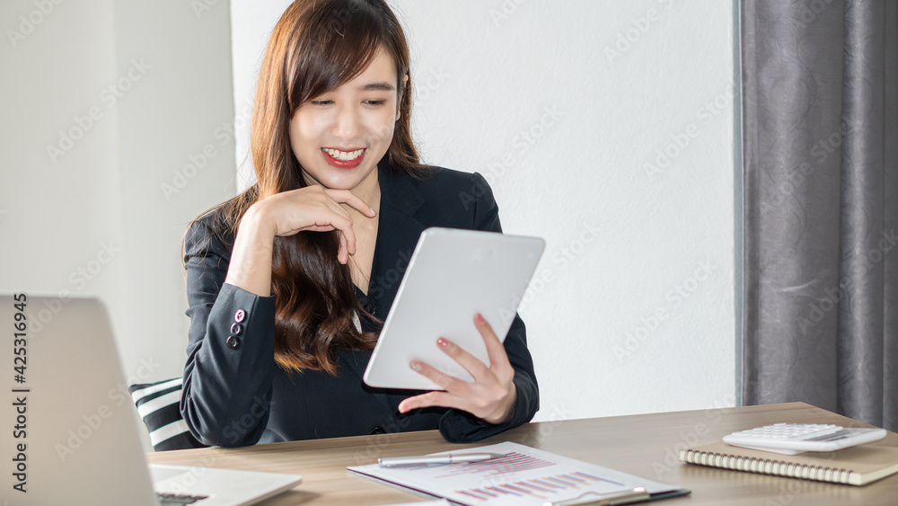 Young Asian businesswoman happily working on documents, graphs and laptops, smiling in the office. Young Asian businesswoman happily working on documents, graphs and laptops, smiling in the office.