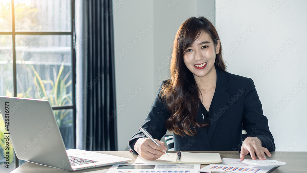 Young Asian businesswoman happily working on documents, graphs and laptops, smiling in the office. Young Asian businesswoman happily working on documents, graphs and laptops, smiling in the office.