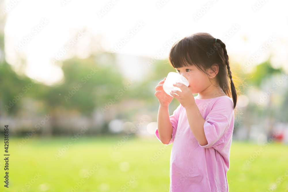Adorable Asian child girl are drinking fresh water from plastic glasses. Green natural background. In the summer or spring. Side view of kid is 4 year old wearing pink shirt thirsty. Adorable Asian child girl are drinking fresh water from plastic glasses. Green natural background. In the summer or spring. Side view of kid is 4 year old wearing pink shirt thirsty.