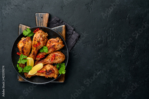 Grilled chicken drumsticks or legs or roasted bbq with spices and tomato salsa sauce on a black plate. Top view with copy space.
