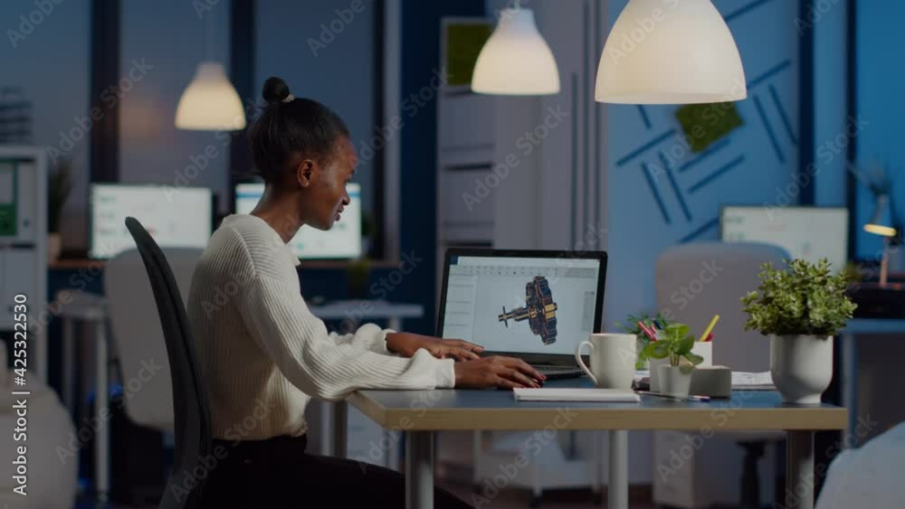 African engineer working late at night on a 3D model of industrial gears at laptop doing overtime in start up office. Freelancer studying prototype idea on pc showing cad software on device display African engineer working late at night on a 3D model of industrial gears at laptop doing overtime in start up office. Freelancer studying prototype idea on pc showing cad software on device display