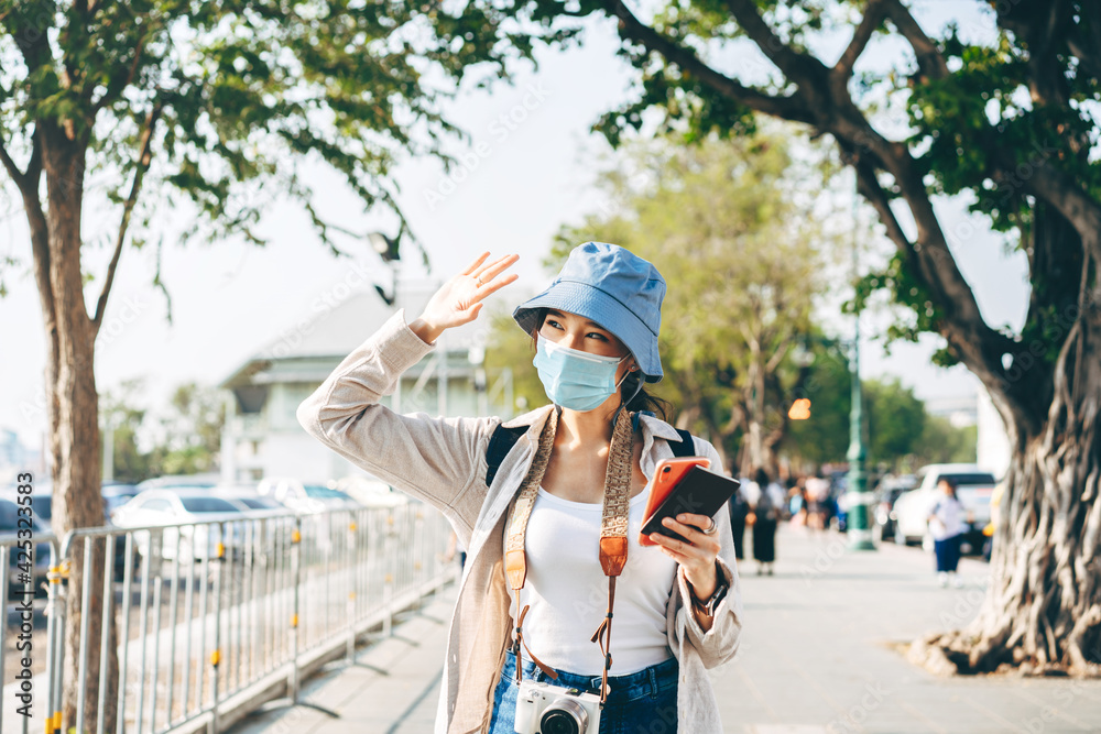 Walking young adult asian woman traveller wear face mask for covid-19 traveling in local city on summer day.