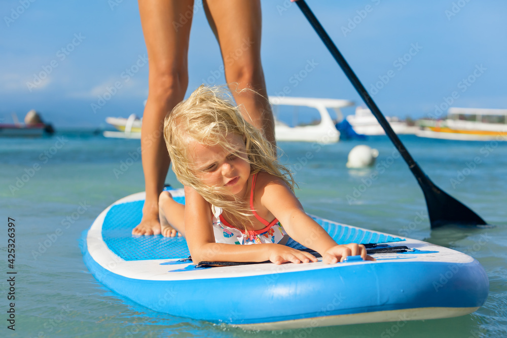 Active paddle boarder at sunset sea. Young mother with little clild paddling on stand up paddleboard. Healthy lifestyle. Water sport, SUP surfing tour in adventure camp on family summer beach vacation