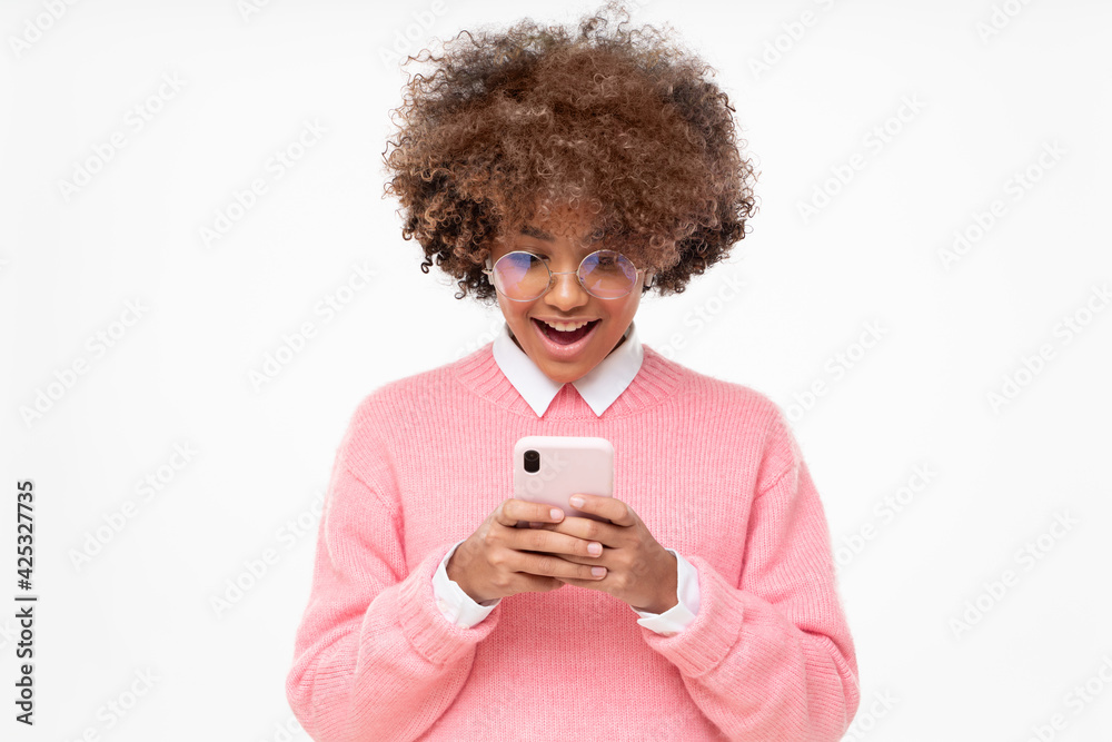 Shocked happy african girl with wow face, holding phone with both hands, surprised by message from friend, isolated on gray background Shocked happy african girl with wow face, holding phone with both hands, surprised by message from friend, isolated on gray background