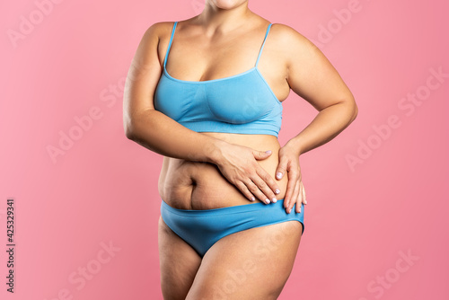 Fat woman in blue underwear on pink background, overweight female body
