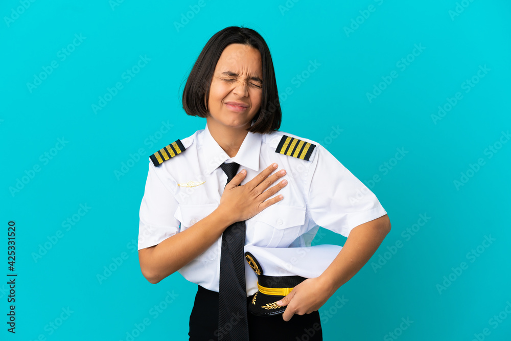 Young airplane pilot over isolated blue background having a pain in the heart Young airplane pilot over isolated blue background having a pain in the heart