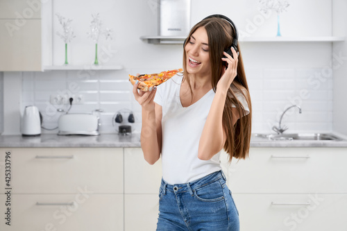 Young woman standing in kitchen and eating pizza.