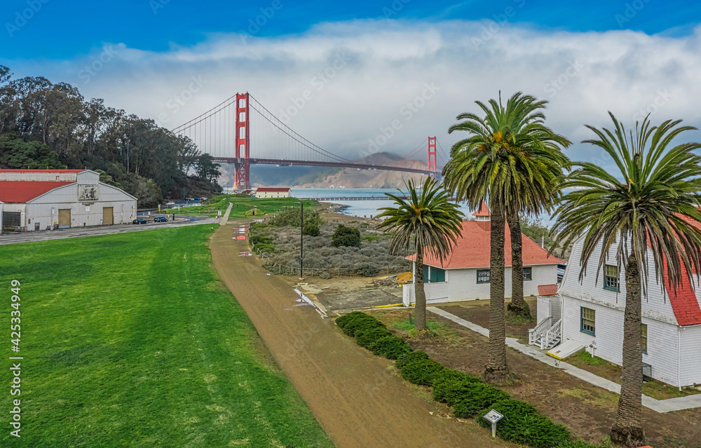 Aerial view of the Golden Gate Bridge from Presidio, against the backdrop, of beautiful palm trees, in San Francisco, bright sunny weather, palm trees and green grass on the lawn.