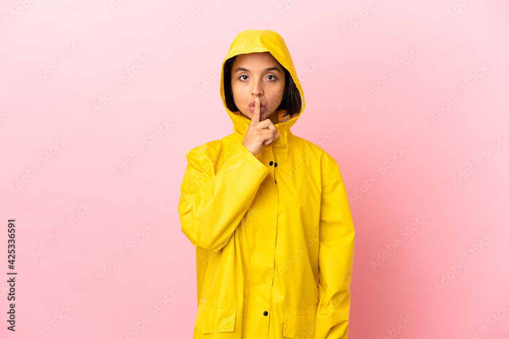Young latin woman wearing a rainproof coat over isolated background showing a sign of silence gesture putting finger in mouth Young latin woman wearing a rainproof coat over isolated background showing a sign of silence gesture putting finger in mouth
