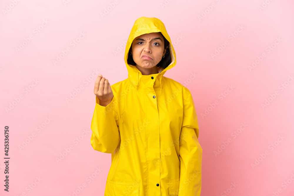 Young latin woman wearing a rainproof coat over isolated background making Italian gesture