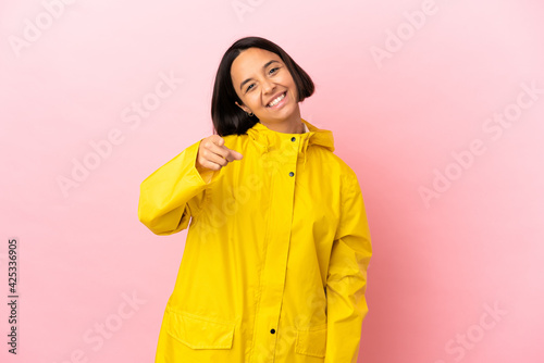 Young latin woman wearing a rainproof coat over isolated background pointing front with happy expression