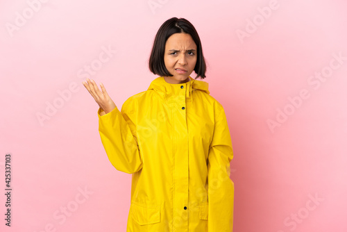 Young latin woman wearing a rainproof coat over isolated background having doubts © luismolinero