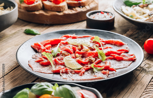 Black plate with carpaccio of beef with baby arugul and lime on rustic wooden background.