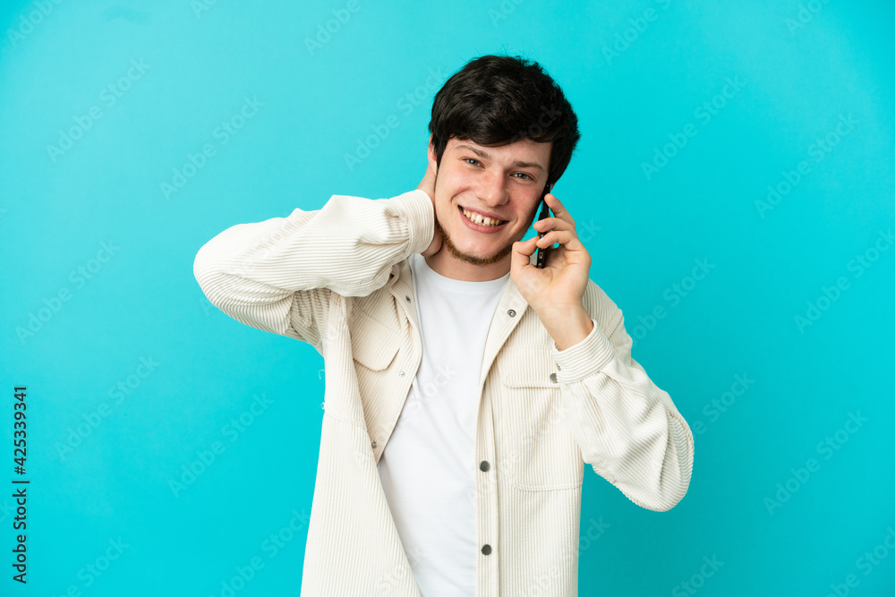 Young Russian man using mobile phone isolated on blue background laughing Young Russian man using mobile phone isolated on blue background laughing