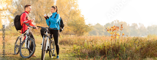 Obraz na płótnie Wide aspect ratio, panoramic photo of a young Caucasian man and woman eating energy bars and talking while resting from a mountain bike ride in countryside w salonie