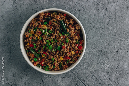 Fried Rice with vegetables, green onion and sesame in white bowl on stone background.