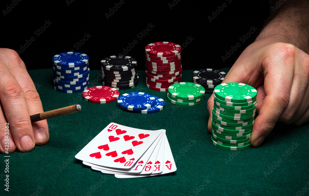 Hands of a gambler closeup and chips on green table in a poker club. A player places a bet on winning poker royal flush Hands of a gambler closeup and chips on green table in a poker club. A player places a bet on winning poker royal flush