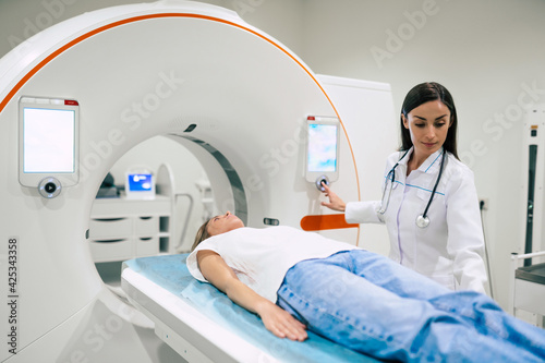 Professional Doctor Radiologist In Medical Laboratory Controls magnetic resonance imaging or computed tomography or PET Scan with Female Patient Undergoing Procedure.