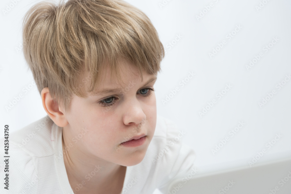 The blond child looks attentively at the computer or laptop screen. Close-up portrait The blond child looks attentively at the computer or laptop screen. Close-up portrait