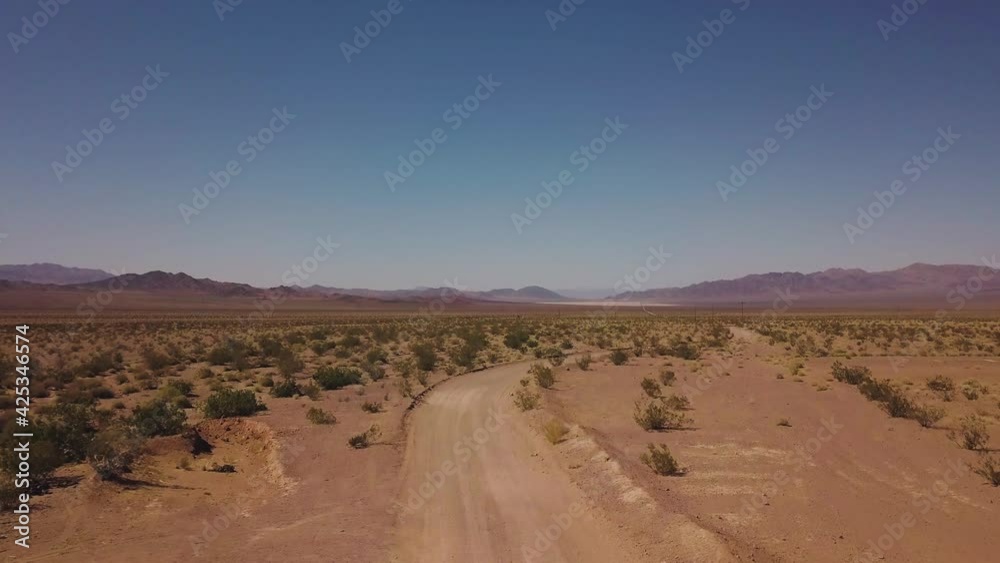 Lonely desert dirt road reveals a red mountain range in the distance, with a gate in the foreground, and scrubland - Drone push forward and reveal - Arizona USA Lonely desert dirt road reveals a red mountain range in the distance, with a gate in the foreground, and scrubland - Drone push forward and reveal - Arizona USA