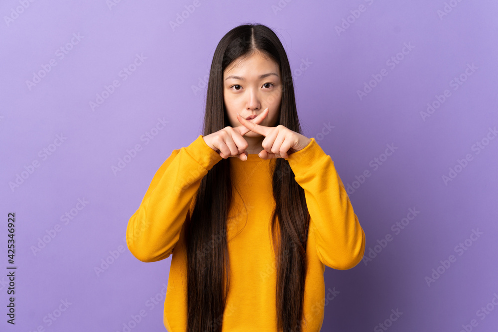 Young Chinese girl over isolated purple background showing a sign of silence gesture Young Chinese girl over isolated purple background showing a sign of silence gesture