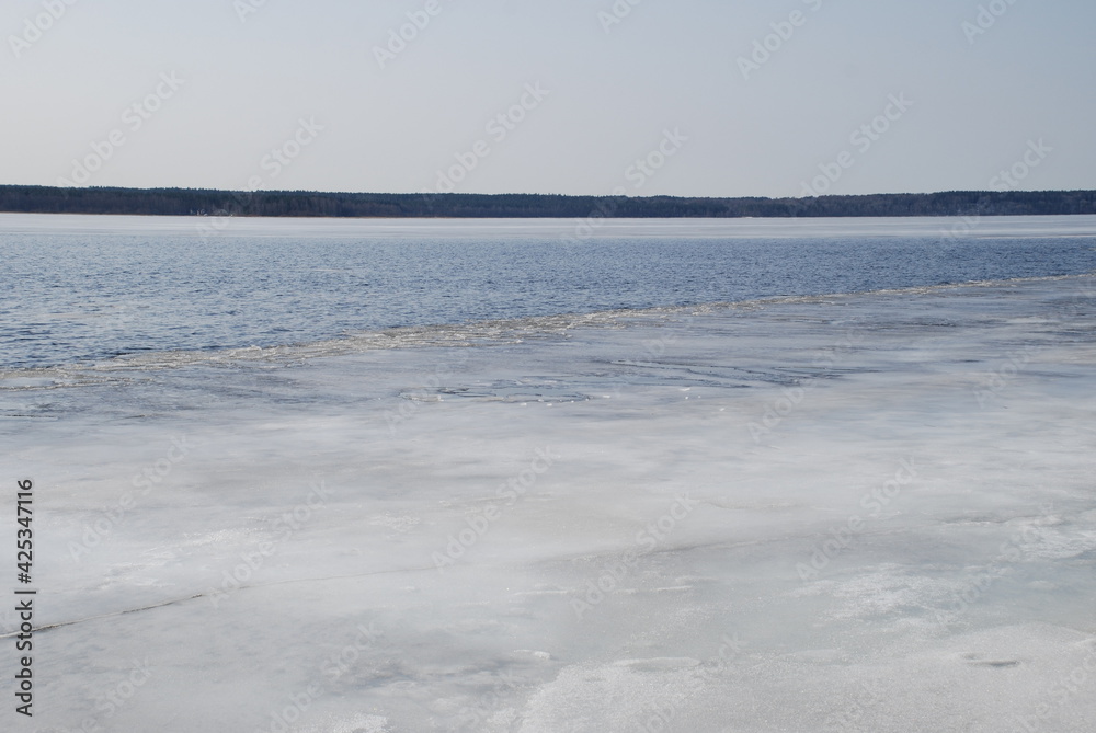 A river is being freed from ice. Spring day light blue sky, river flood with blue water. At the very shore there is a small strip of ice, the middle of the river is without ice. On other side trees A river is being freed from ice. Spring day light blue sky, river flood with blue water. At the very shore there is a small strip of ice, the middle of the river is without ice. On other side trees