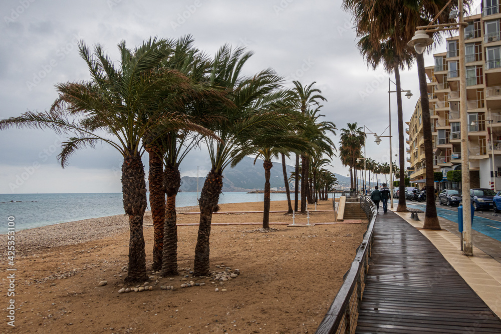 Altea beach, with palm trees, and people walking along a wooden walkway, on a rainy day.