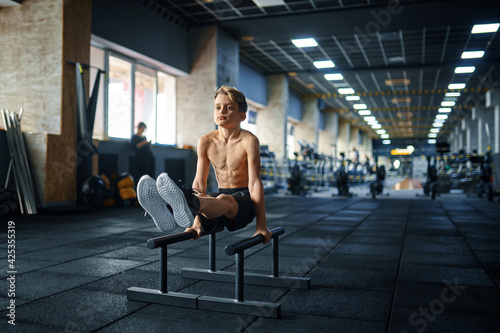 Boy doing ABS exercise on uneven bars in gym