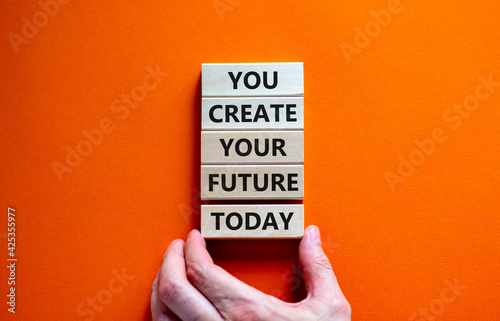 You create your future today symbol. Concept words 'You create your future today' on wooden blocks on a beautiful orange background. Businessman hand. Business, motivational and create future concept.