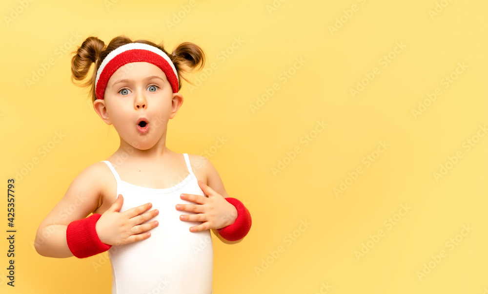 Excited fitness child posing in sportswear,red wristbands,headband over yellow studio background. Children sport,advertising,shopping concept.Gym workout.Childhood activity.Sport.Health and energy Excited fitness child posing in sportswear,red wristbands,headband over yellow studio background. Children sport,advertising,shopping concept.Gym workout.Childhood activity.Sport.Health and energy