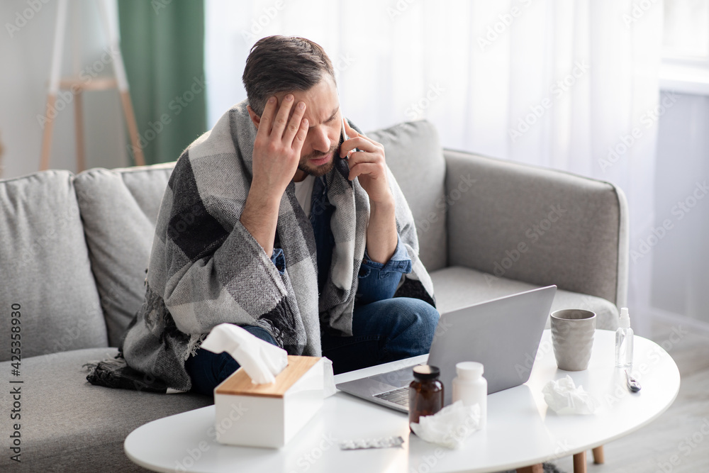 Sick man working on laptop at home, talking on phone Sick man working on laptop at home, talking on phone