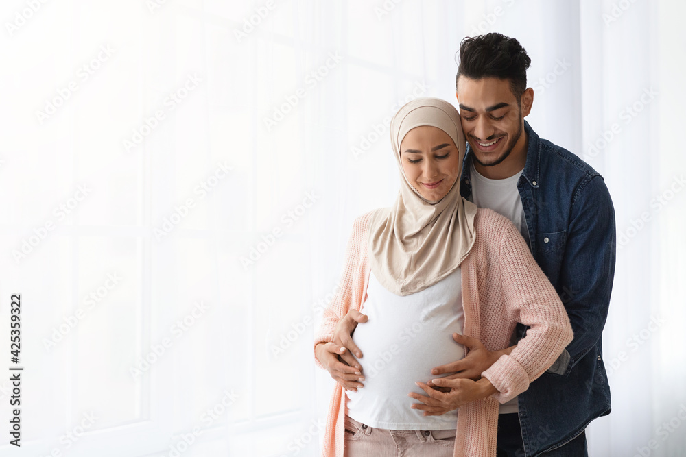 Muslim Family Expecting Baby. Caring arab husband embracing pregnant wife's belly Muslim Family Expecting Baby. Caring arab husband embracing pregnant wife's belly
