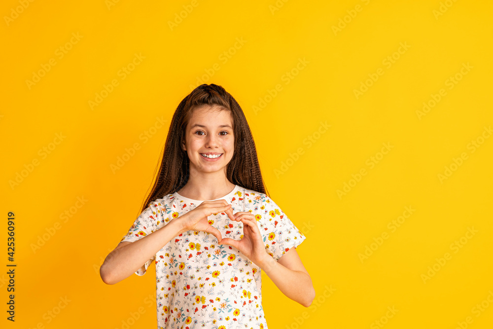 portrait of a happy cute young girl making a heartfelt gesture, isolated on a yellow studio background. Smiling brown-haired 5 years old charming contented cutie shows a sign of love. portrait of a happy cute young girl making a heartfelt gesture, isolated on a yellow studio background. Smiling brown-haired 5 years old charming contented cutie shows a sign of love.