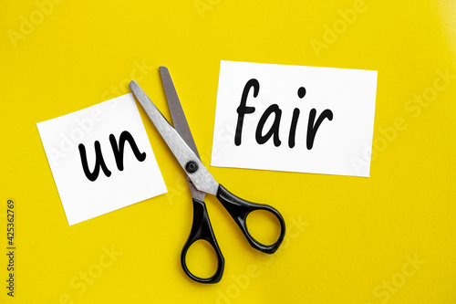 Photography Cutting Unfair to Fair Paper Sign with Scissors on a yellow background