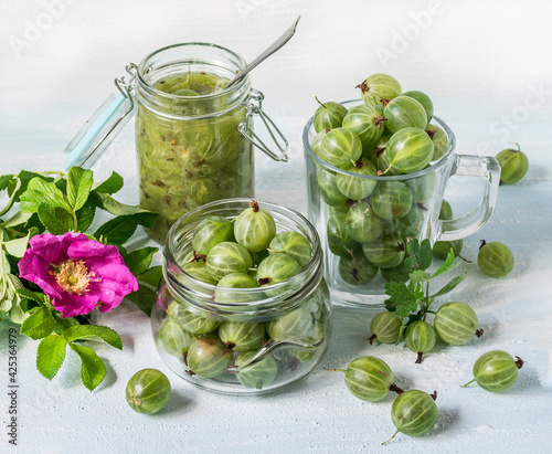 A small glass jar with homemade jam and the fresh gooseberry berries on a white background. Selective focus.