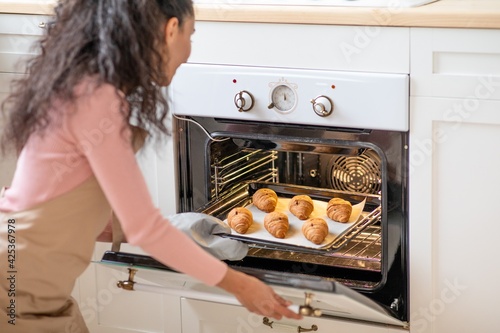 Unrecognizable Young Woman Taking Tray With Croissants Out Of Oven On Kitchen