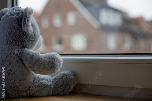 Stuffed animal looking out of a window, symbolizing isolated children during lockdown or quarantine during the corona pandemic photo