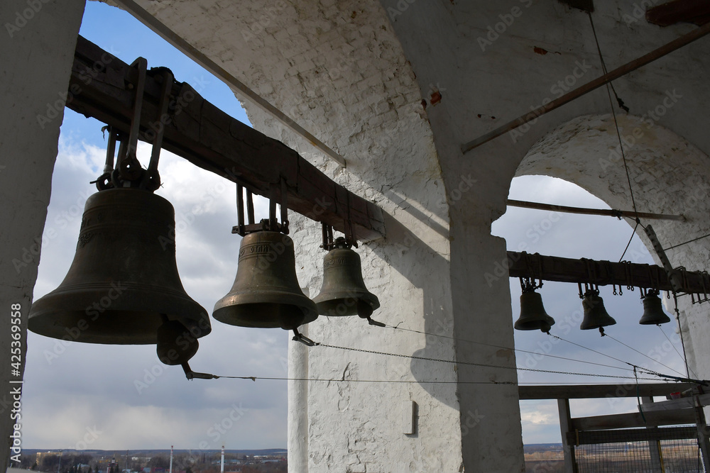 Bells in the vaults on the bell tower on the blurred background of the sky and the city