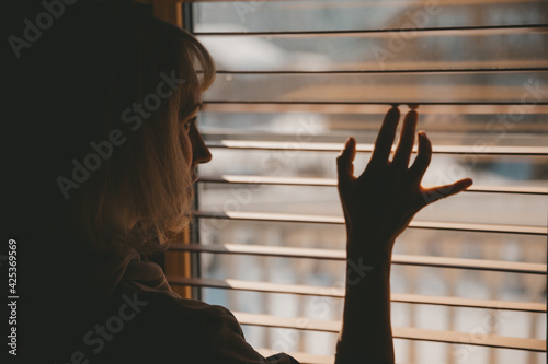 Fotografie A woman looks out the window through the blinds