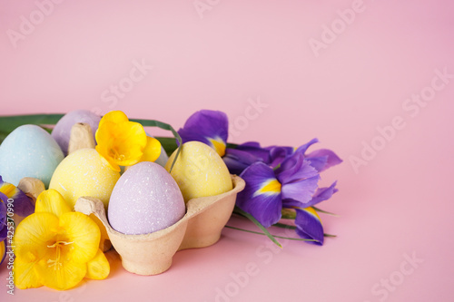 Colorful Easter eggs in a tray and flowers on a pink background. Place for text