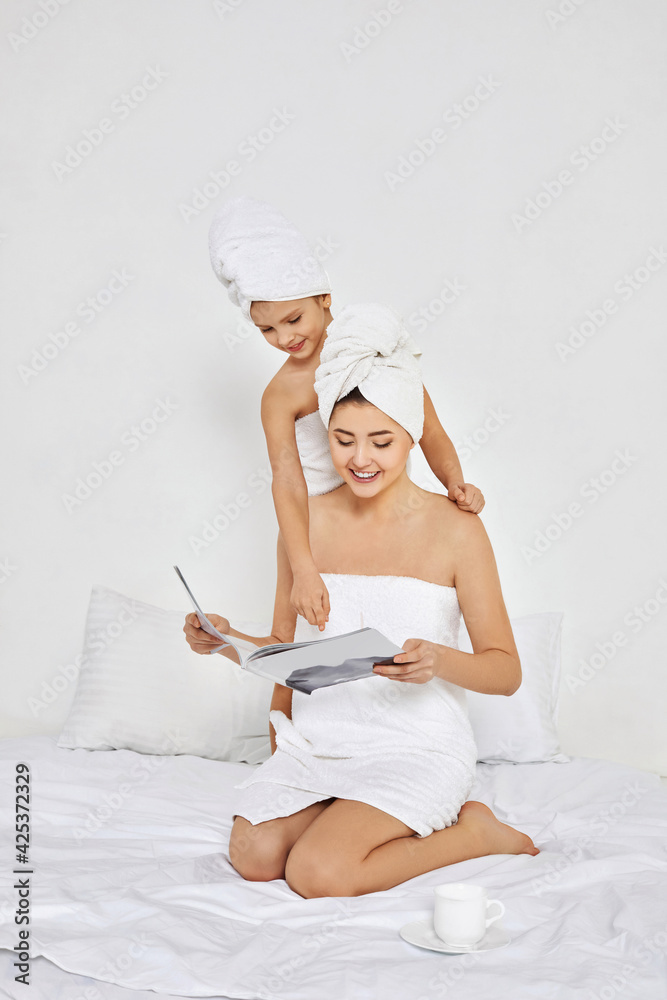 mother and little daughter in white bathrobes read magazines mother and little daughter in white bathrobes read magazines